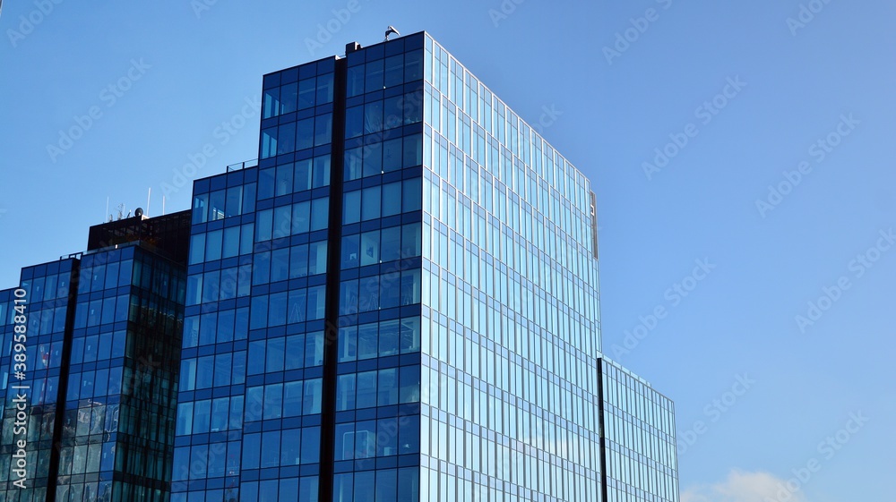 Blue curtain wall made of toned glass and steel constructions under blue sky. A fragment of a building. Blue curtain wall made of toned glass and steel constructions under blue sky. A fragment of a building.