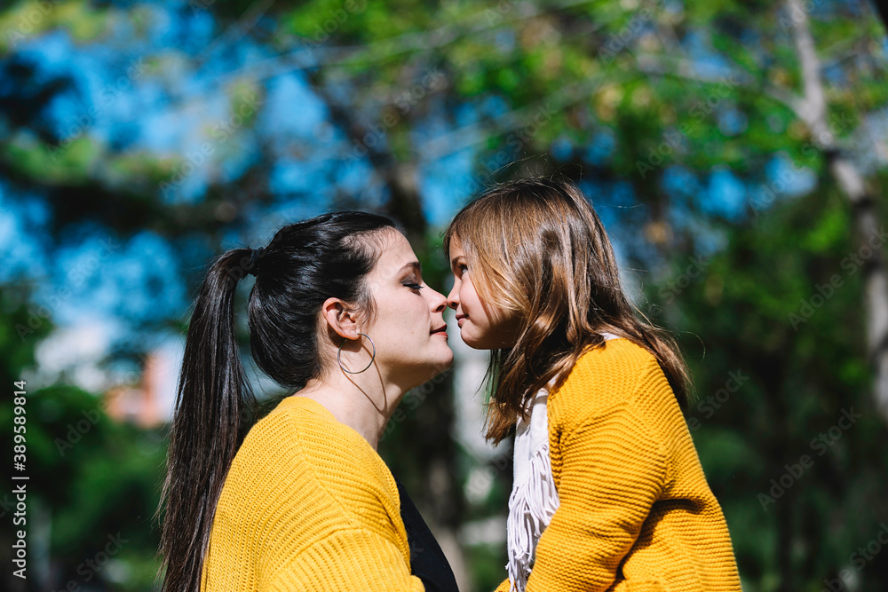 Fototapeta premium Little cute child baby girl kiss on cheek and hug, embrace with happy pretty woman in green park. Mother, little kid daughter. Mother's Day, love family, parenthood, childhood