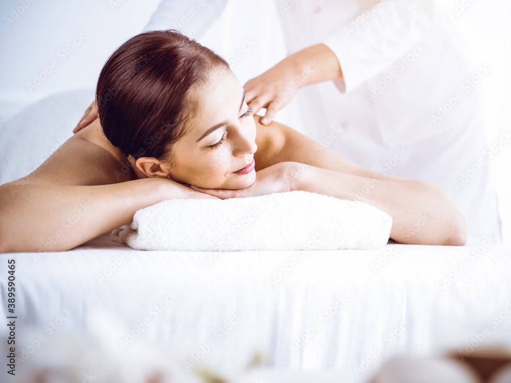 Beautiful brunette woman enjoying back massage in sunny spa center. Beauty and medicine concept Beautiful brunette woman enjoying back massage in sunny spa center. Beauty and medicine concept