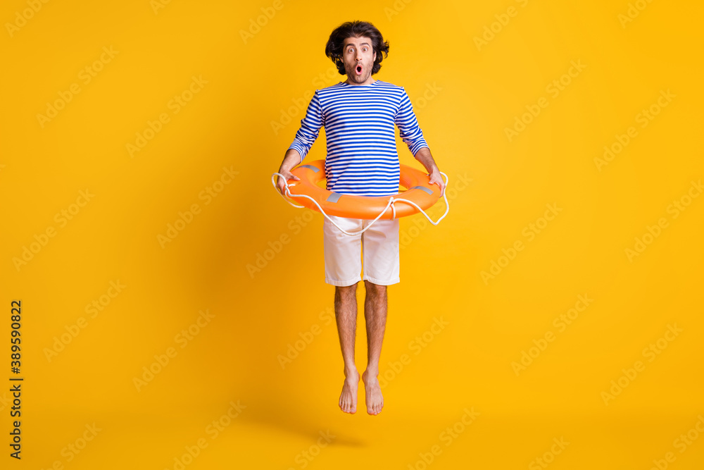 Full body photo of shocked guy jump up wear orange rubber lifesaver shorts  blue white shirt isolated on yellow color background Stock Photo