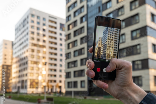 Real estate agent taking a photo of property with his smartphone. Close-up of hands of realtor with the phone taking pictures of new residential building photo