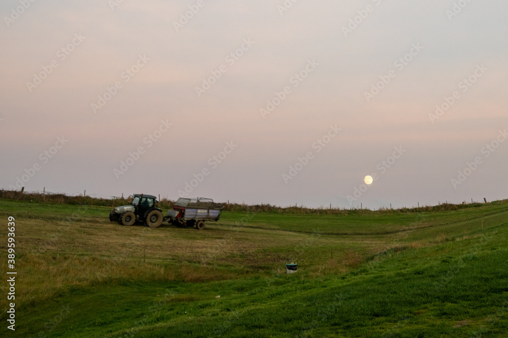 farmer with tractor and trailer cultivating fields under a full moon at sunset farmer with tractor and trailer cultivating fields under a full moon at sunset