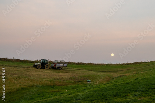 farmer with tractor and trailer cultivating fields under a full moon at sunset © makasana photo