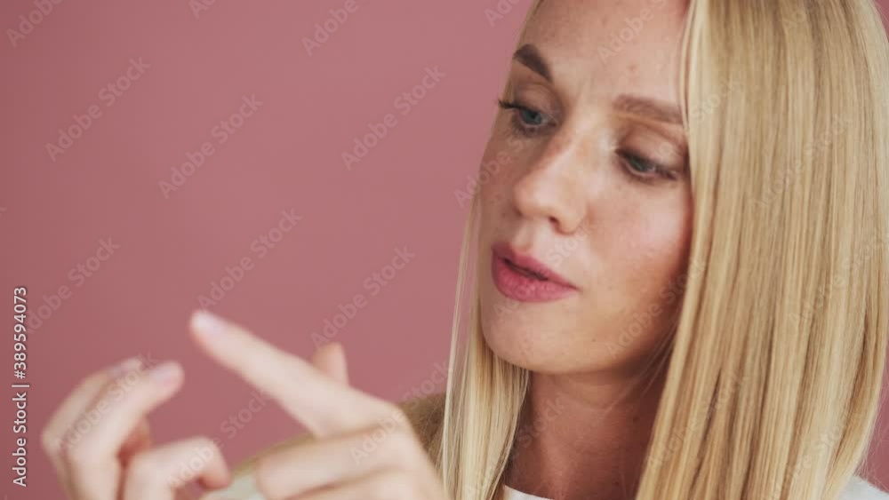 A happy blonde woman is counting on her fingers standing isolated over pink background in studio A happy blonde woman is counting on her fingers standing isolated over pink background in studio