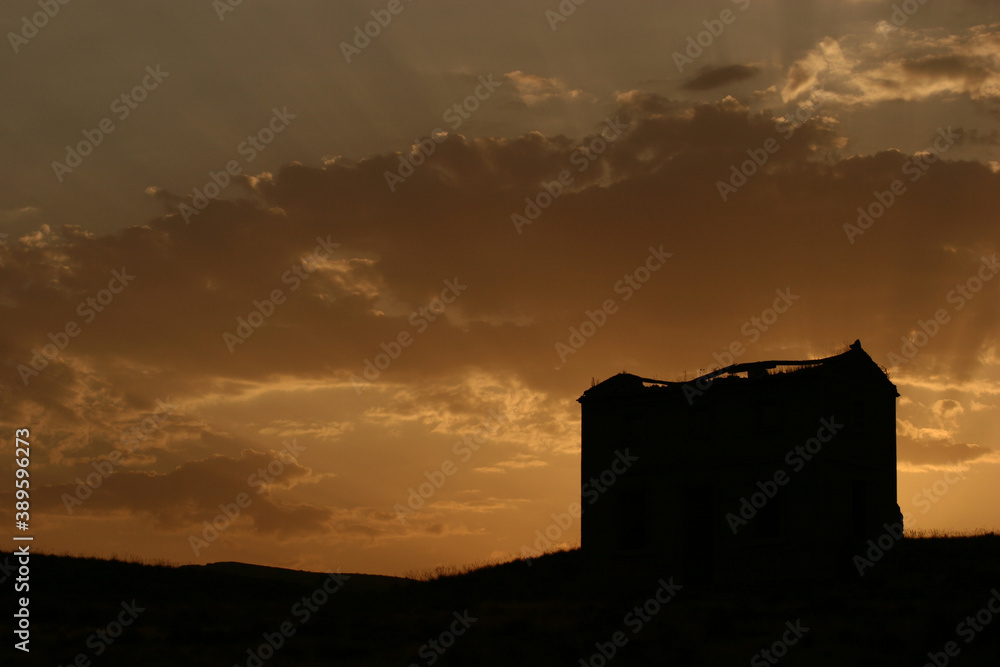 Casa en ruinas en el campo a contraluz durante el atardecer, con nubes en el cielo.