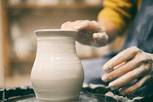 Woman makes pottery making in the workshop on a potter's wheel, hands in clay close-up photo