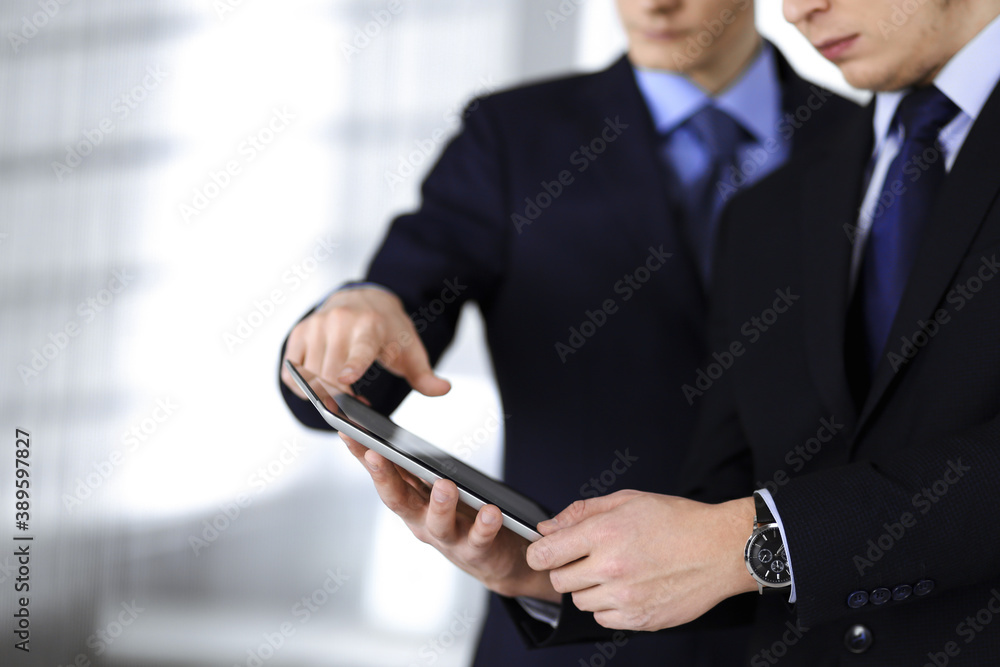 Business people use a tablet computer for discussion of their new project, standing in a modern office. Unknown businessman or male entrepreneur with a colleague at workplace. Teamwork and partnership Business people use a tablet computer for discussion of their new project, standing in a modern office. Unknown businessman or male entrepreneur with a colleague at workplace. Teamwork and partnership