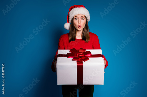 Photo of astonished girl in santa claus cap receive big gift box x-mas christmas newyear party midnight impressed wear trendy knitted pullover isolated dark blue color background