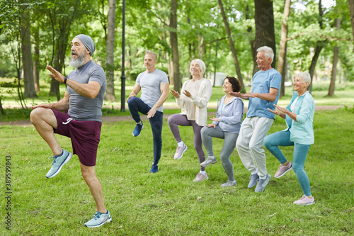 Wide shot of active elderly men and women doing morning workout in park with senior trainer © Seventyfour