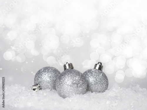 Three silver Christmas balls in the snow on an abstract bokeh background.