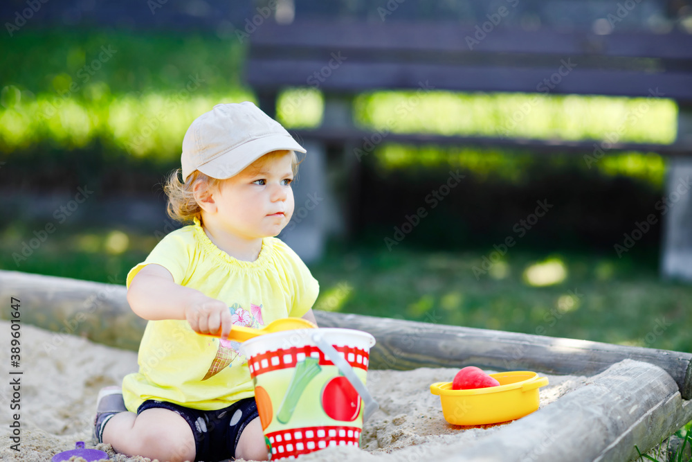 Cute toddler girl playing in sand on outdoor playground. Beautiful baby having fun on sunny warm summer sunny day. Happy healthy child with sand toys and in colorful fashion clothes. Cute toddler girl playing in sand on outdoor playground. Beautiful baby having fun on sunny warm summer sunny day. Happy healthy child with sand toys and in colorful fashion clothes.