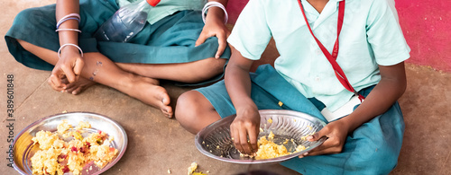 Unidentified poor classmates children with uniforms sitting on the floor outdoors, eating with their right hand some rice with masala. Lunch time photo