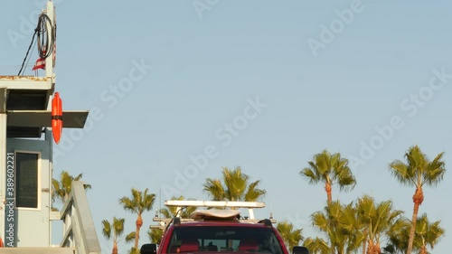 Iconic retro wooden lifeguard watch tower, baywatch red car. Life buoy, american state flag and palm trees against blue sky. Summertime california aesthetic, Santa Monica beach, Los Angeles, CA USA.