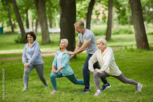 Group of three senior women spending morning together in park doing exercises with their trainer helping them