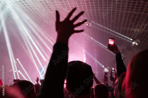 A crowd of people at the concert have fun and dance to the music at the concert. Rear view. Hand close up. The concept of entertainment and relaxation