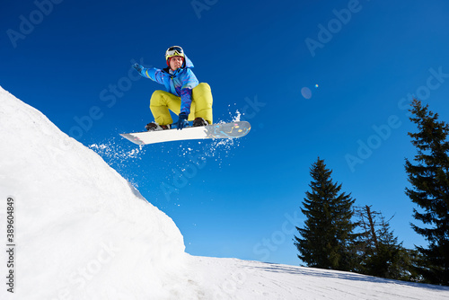 Jumping snowboarder keeps one hand on the snowboard on blue sky background. Ski season and winter sports concept