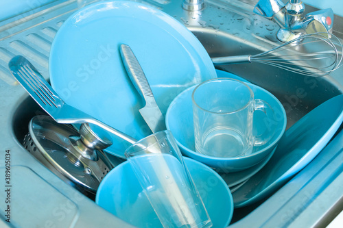 dishes in the sink close up, blue plates, stainless steel knife, bowls, glasses