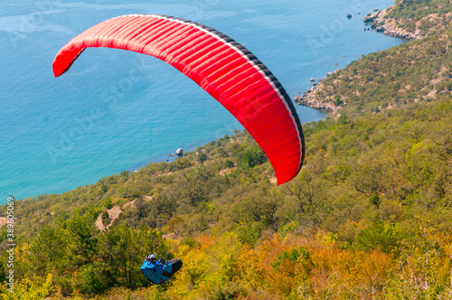 a man flies on a paraglider over a mountain in greenery and a blue sea photo