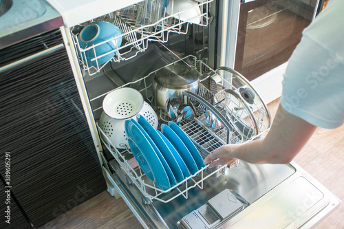 Female inserts the lower basket of the dishwasher by left hand. Clean dishes: bowls, glasses, plates, left view