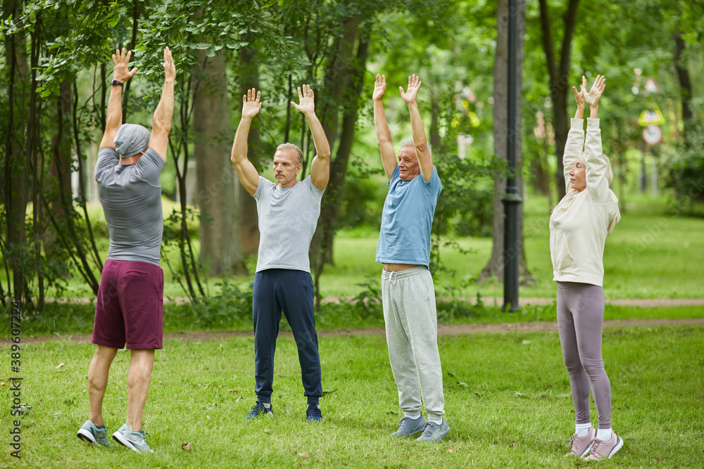Wide shot of active senior people doing hands up stretching exercise in front of their trainer in city park Wide shot of active senior people doing hands up stretching exercise in front of their trainer in city park