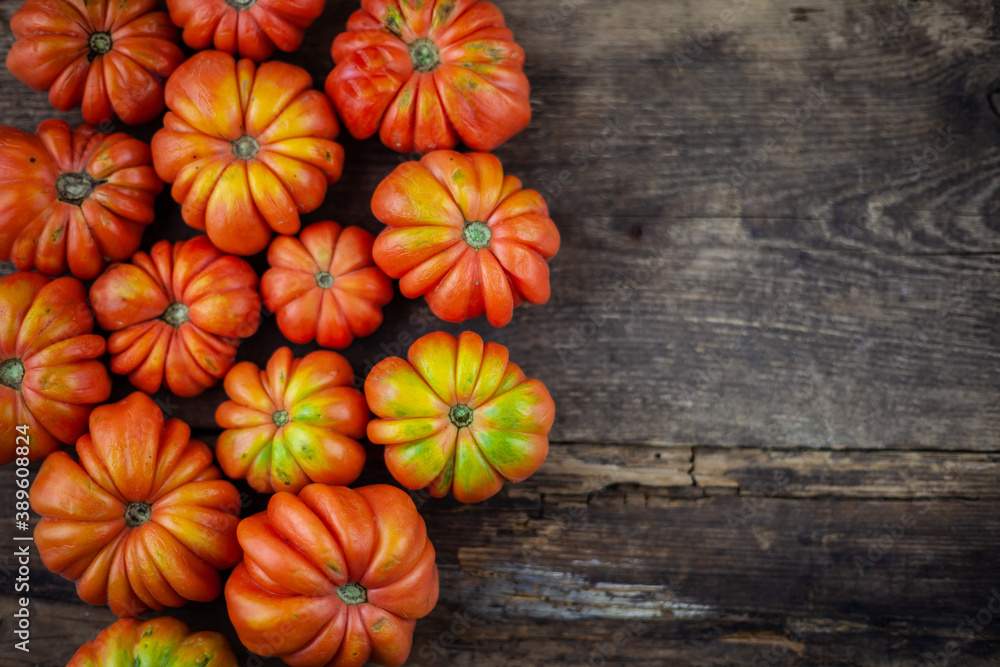 Red ribbed tomatoes on a wooden background. American or Florentine variety Nina. Tomato top view. Food on the table. Place for your text. Autumn harvest of vegetables similar to flowers and pumpkins