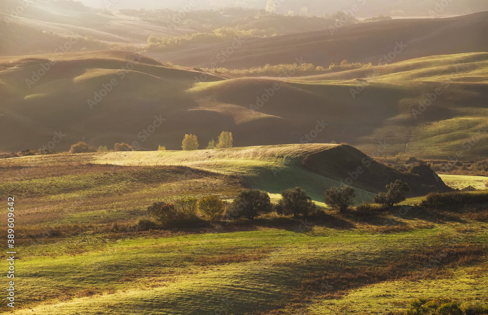 Beautiful Tuscany hills misty morning landscape view. Sunrise light covering the meadows and fields making a magic light-shadows gradients.