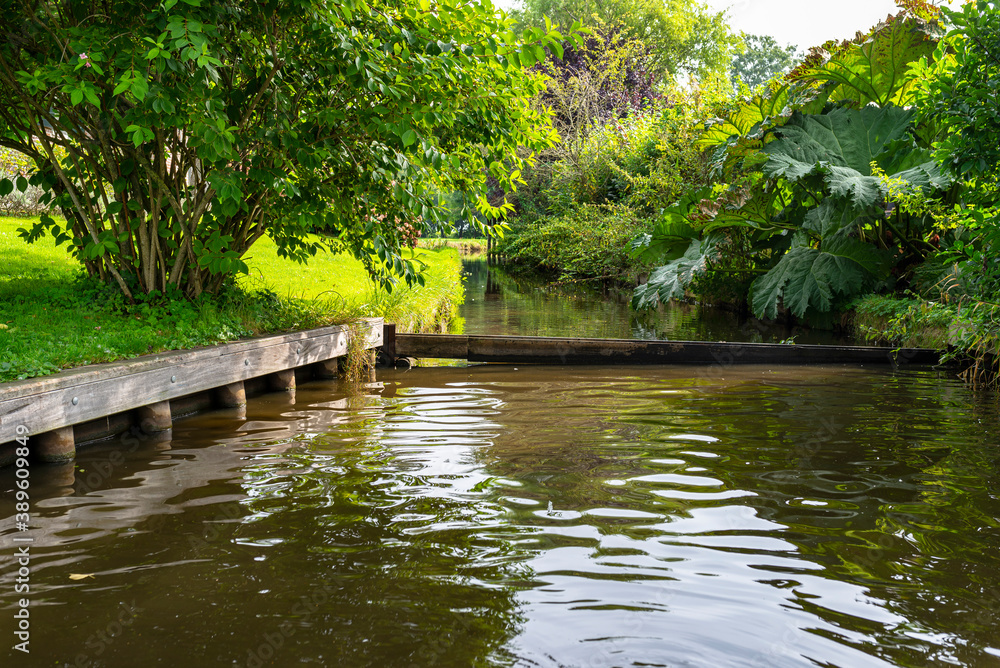 A canal flowing between buildings in a famous village in the Netherlands, visible trees and flowers in the gardens. A canal flowing between buildings in a famous village in the Netherlands, visible trees and flowers in the gardens.