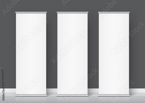 Three white rollup banners standing on the dark grey wall background. The Group of vertical promotional stands for image or text placement. Realistic vector banner template and mockup.