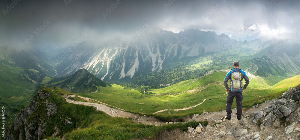 Hiker Man standing in deep hanging clouds above mountains and valley. Mystic light breaks through fog. Tirol, Austria.