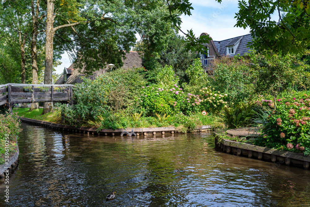 A canal flowing between buildings in a famous village in the Netherlands, visible trees and flowers in the gardens.