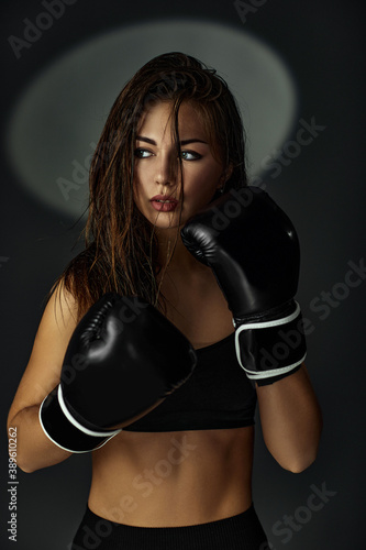 portrait of gorgeous sporty woman in boxing gloves on black studio background © producer