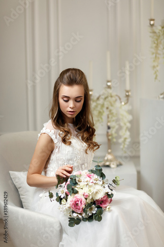 beautiful tender young bride with flower bouquet sitting on armchair in white studio interior