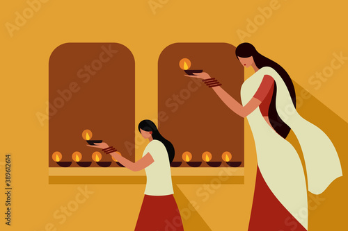 A mother and daughter wearing traditional dress holding lighted Diwali oil lamps in their hands