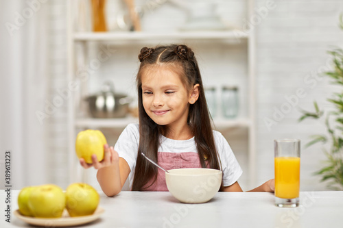 cute little child girl having breakfast - cereal  orange juice and apple in the kitchen. healthy breakfast