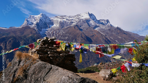 Multi-colored Buddhist prayer flags attached to a pile of stones flying in the wind above village Namche Bazar, Khumbu, Himalayas, Nepal with majestic peak of Kongde Ri (6,187 m) in background.