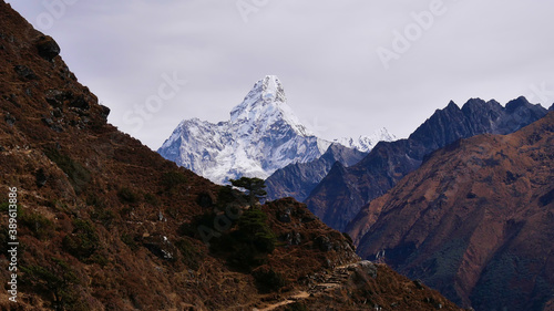 Stunning view of majestic ice-capped mountain Ama Dablam (peak 6,814 m) with footpath in foreground on Everest Base Camp Trek near Namche Bazar, Khumbu, Himalayas, Nepal on cloudy day.