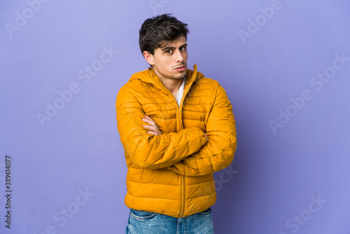 Young cool man frowning face in displeasure, keeps arms folded.