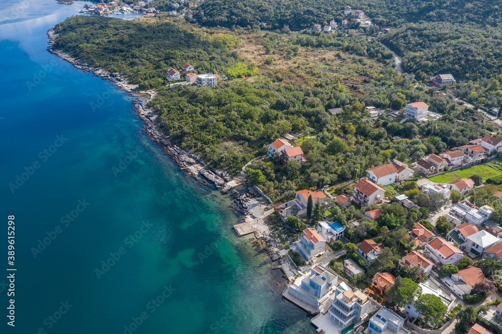 Aerial photo of the coastline of the Adriatic sea bay, small Montenegrin town in autumn. Sunny day, blue sky, mountains are visible in the distance. Water in the sea is turquoise, pure and clear