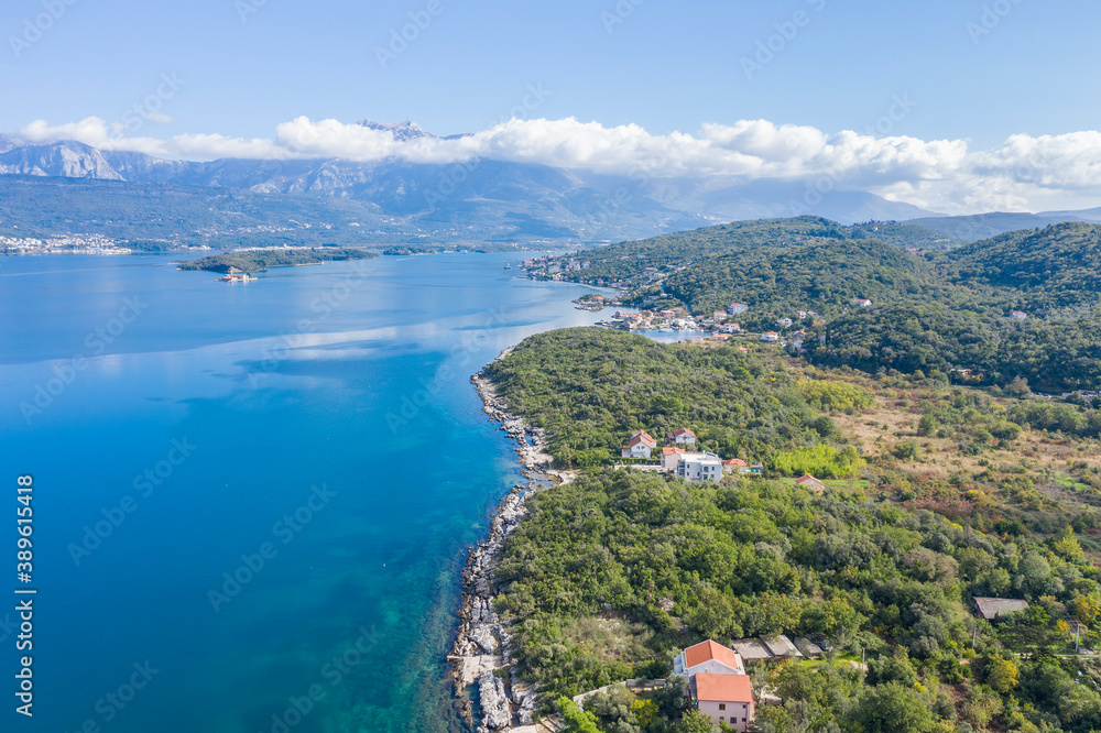 Aerial photo of the coastline of the Adriatic sea bay, small Montenegrin town in autumn. Sunny day, blue sky, mountains are visible in the distance. Water in the sea is turquoise, pure and clear