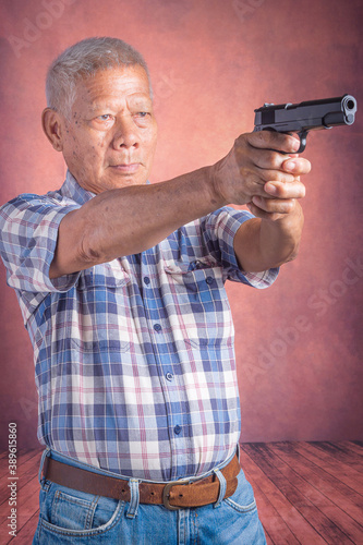 Portrait of an elderly Asian man holding a short gun and looking at the camera while standing with a brown background. Space for text. Concept of aged people and sport