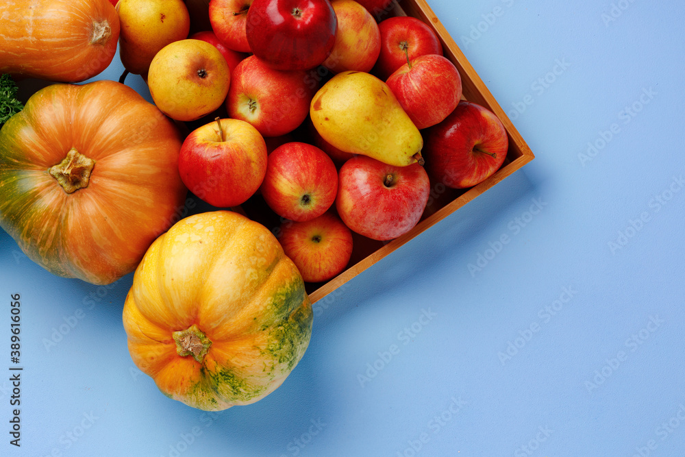 Pumpkins, apples and pears in a wooden box on blue background