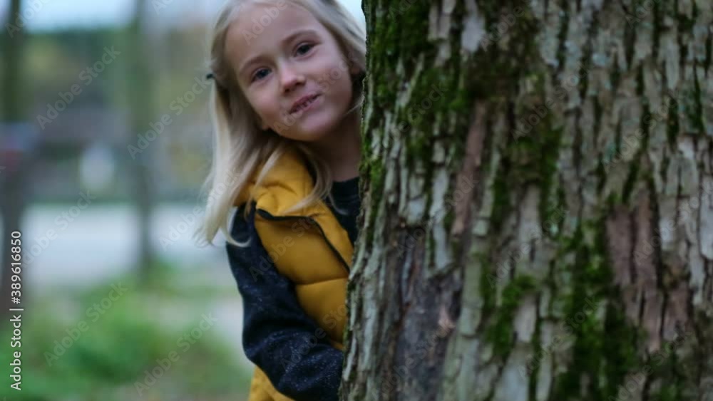 Portrait of a cute little girl. funny girl looks out from behind a tree. playing hide and seek with mom. close up Shot video. Slow motion footage Portrait of a cute little girl. funny girl looks out from behind a tree. playing hide and seek with mom. close up Shot video. Slow motion footage