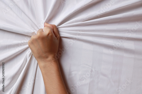 Fotografi Close up young sexy woman hands pulling white sheets in ecstasy in hotel