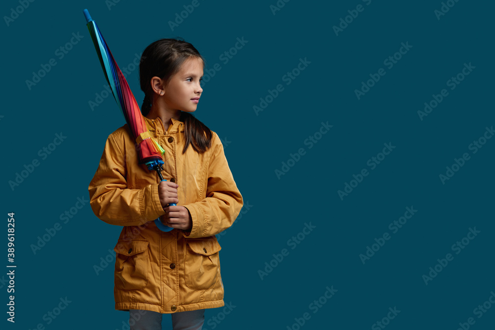 cute child girl with multicolored umbrella in yellow rain coat on blue background. autumn mood. copy space cute child girl with multicolored umbrella in yellow rain coat on blue background. autumn mood. copy space