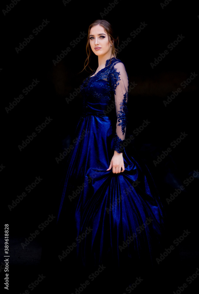 Teen girl in beautiful ultramarine prom dress prom dress. Black background.