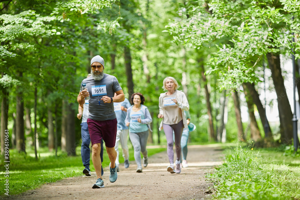 Group of active aged men and women spending day time in park running marathon, wide shot