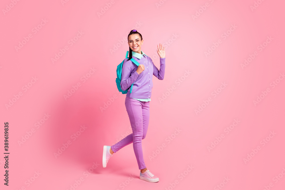 Full length profile photo of cute girl go raise arm palm wear specs rucksack purple jumper pants sneakers isolated pink color background Full length profile photo of cute girl go raise arm palm wear specs rucksack purple jumper pants sneakers isolated pink color background