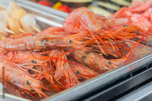 Cooked fresh red langoustine shrimps, prawns and scallop meat in restaurant food container at summer local market - close up. Outdoor cooking, seafood, takeaway, street food concept