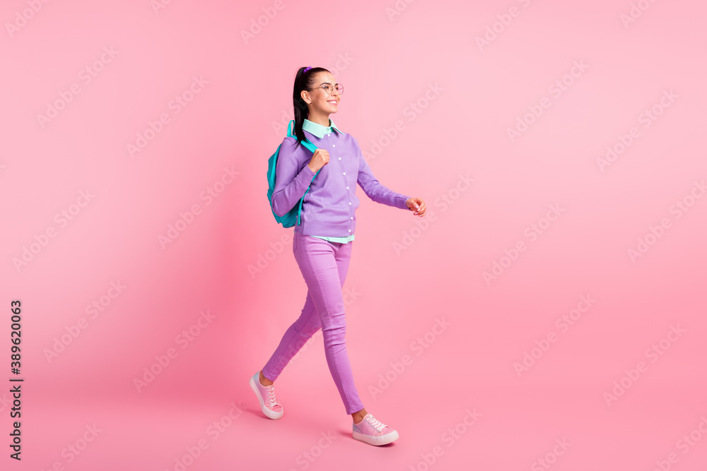 Full length profile photo of lovely lady walk wear specs rucksack purple pullover pants sneakers isolated pink color background