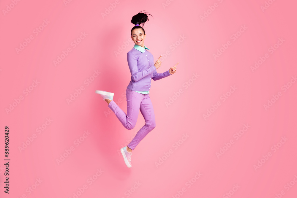 Full length profile photo of sporty girl jump direct fingers empty space wear purple jumper pants sneakers isolated pink color background